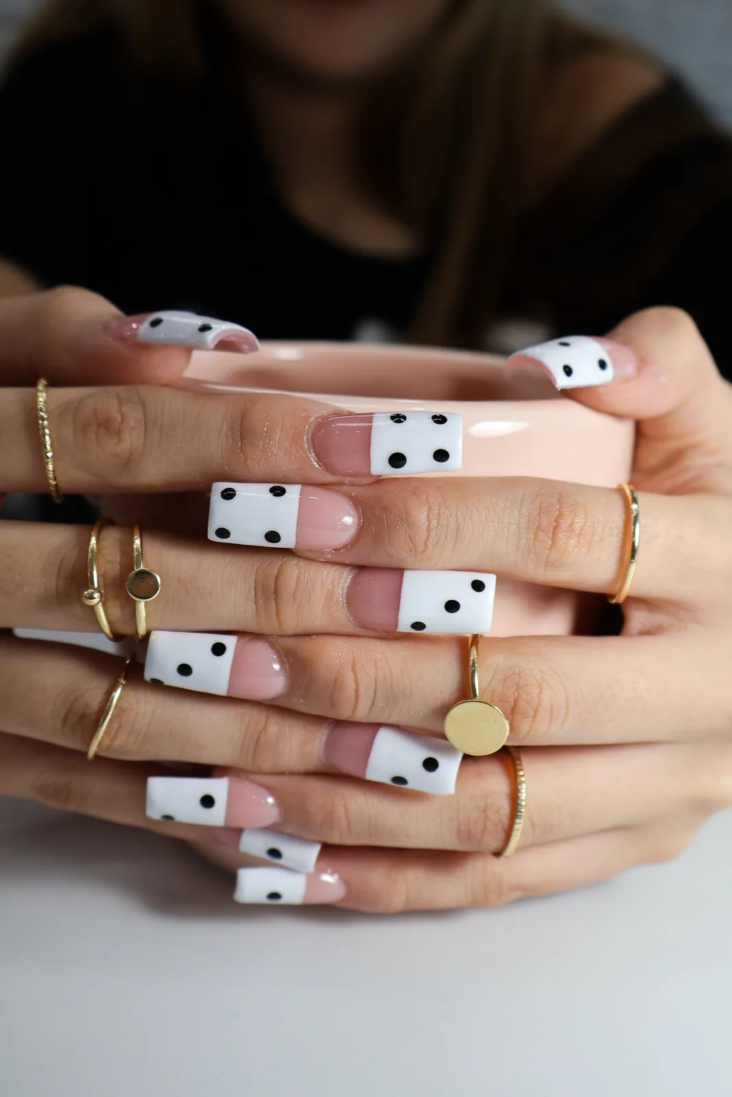 Black polka-dot French nails wrapped around a pink mug