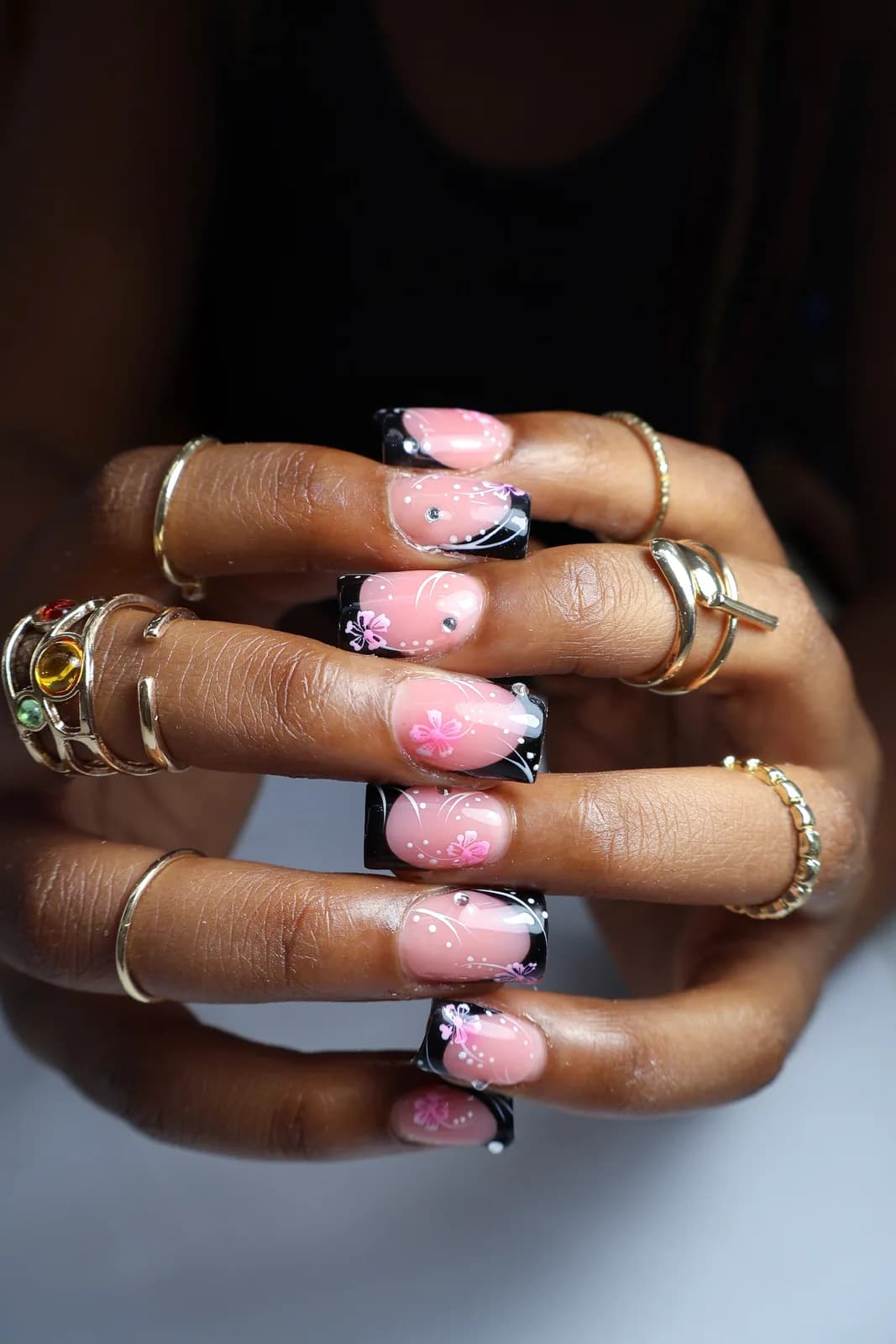 Black French tip nails with white dots, pink flowers, and rhinestones