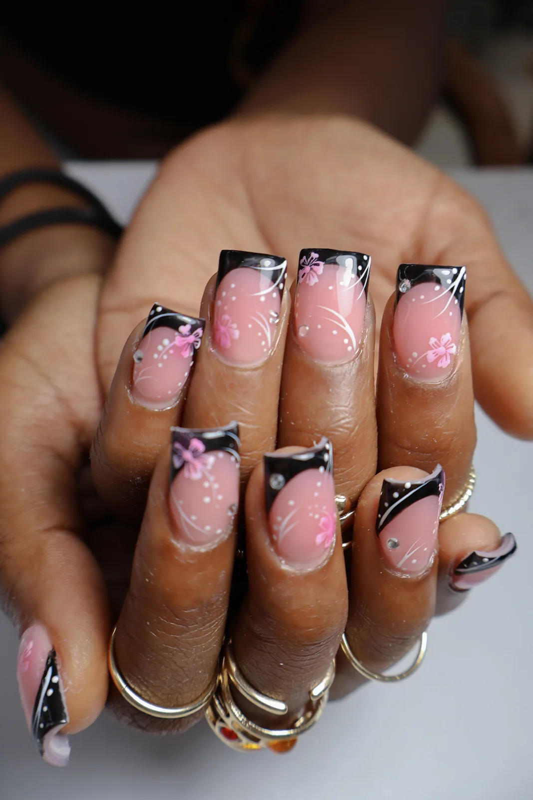 Both hands showing square black French tips with pink floral nail art