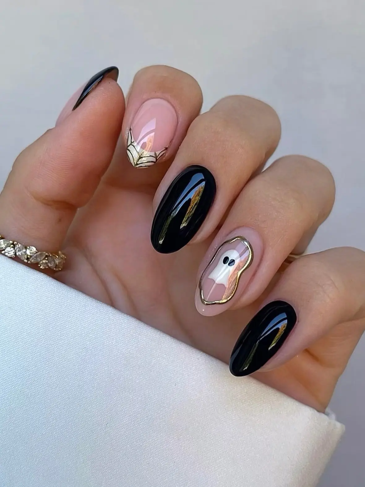 Glossy black almond nails with a gold-outlined ghost accent and a gold cobweb French tip