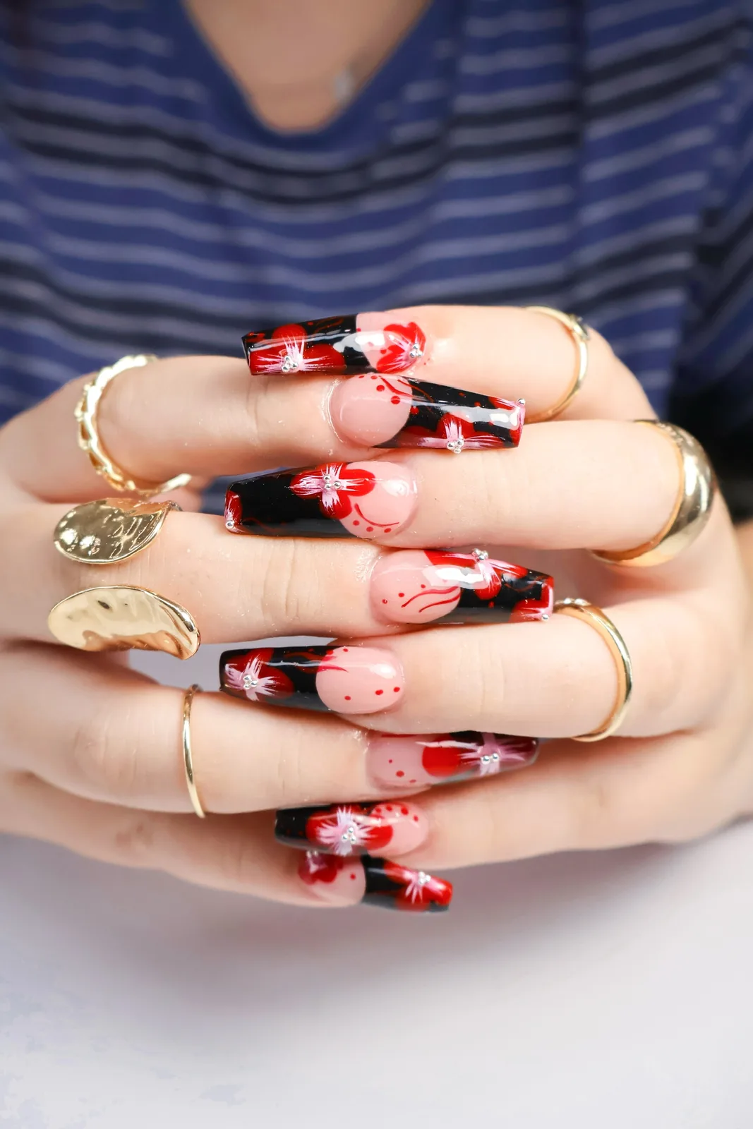 Stacked hands showing long coffin nails with black and red floral nail art