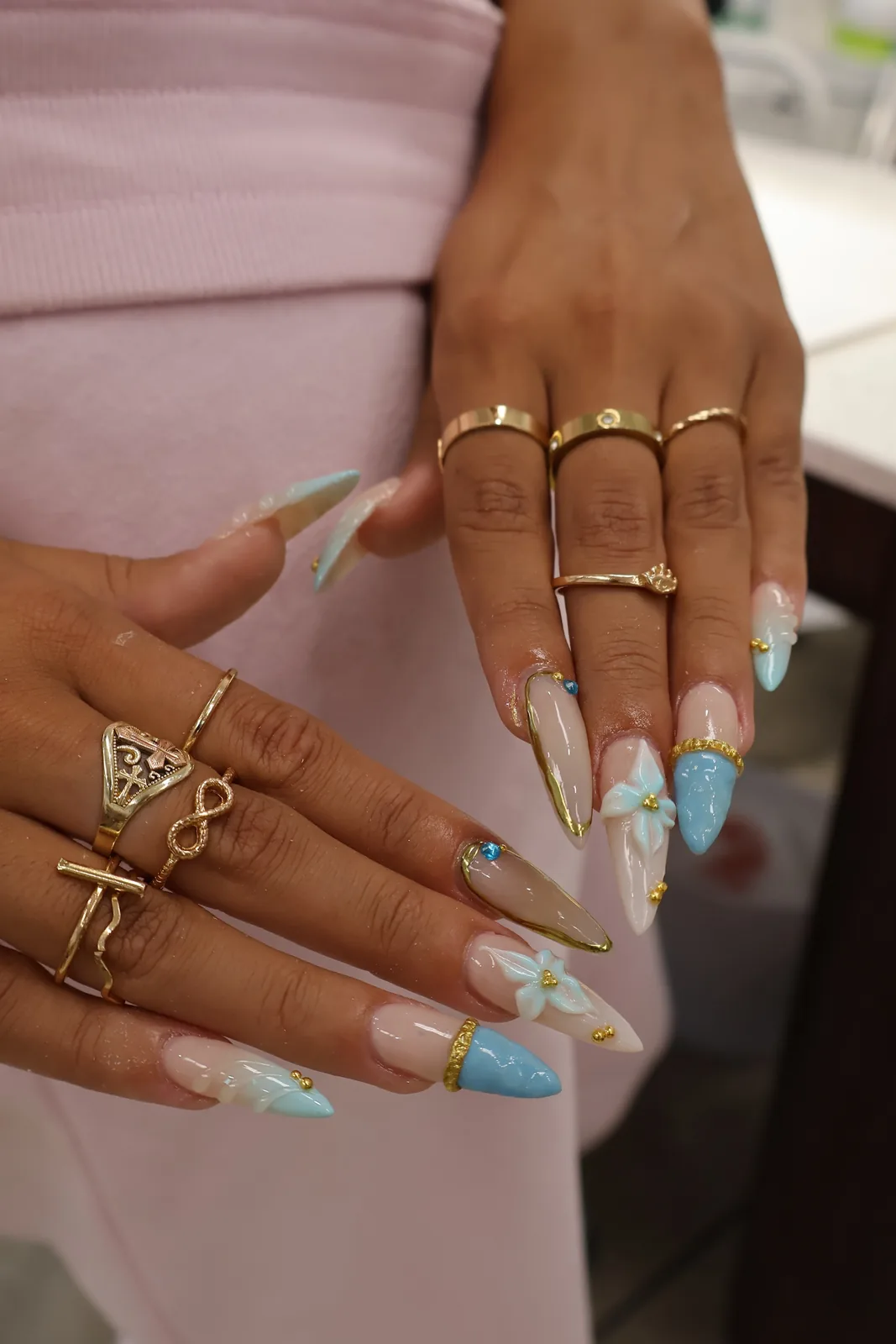 Blue floral stiletto nails styled with stacked gold rings