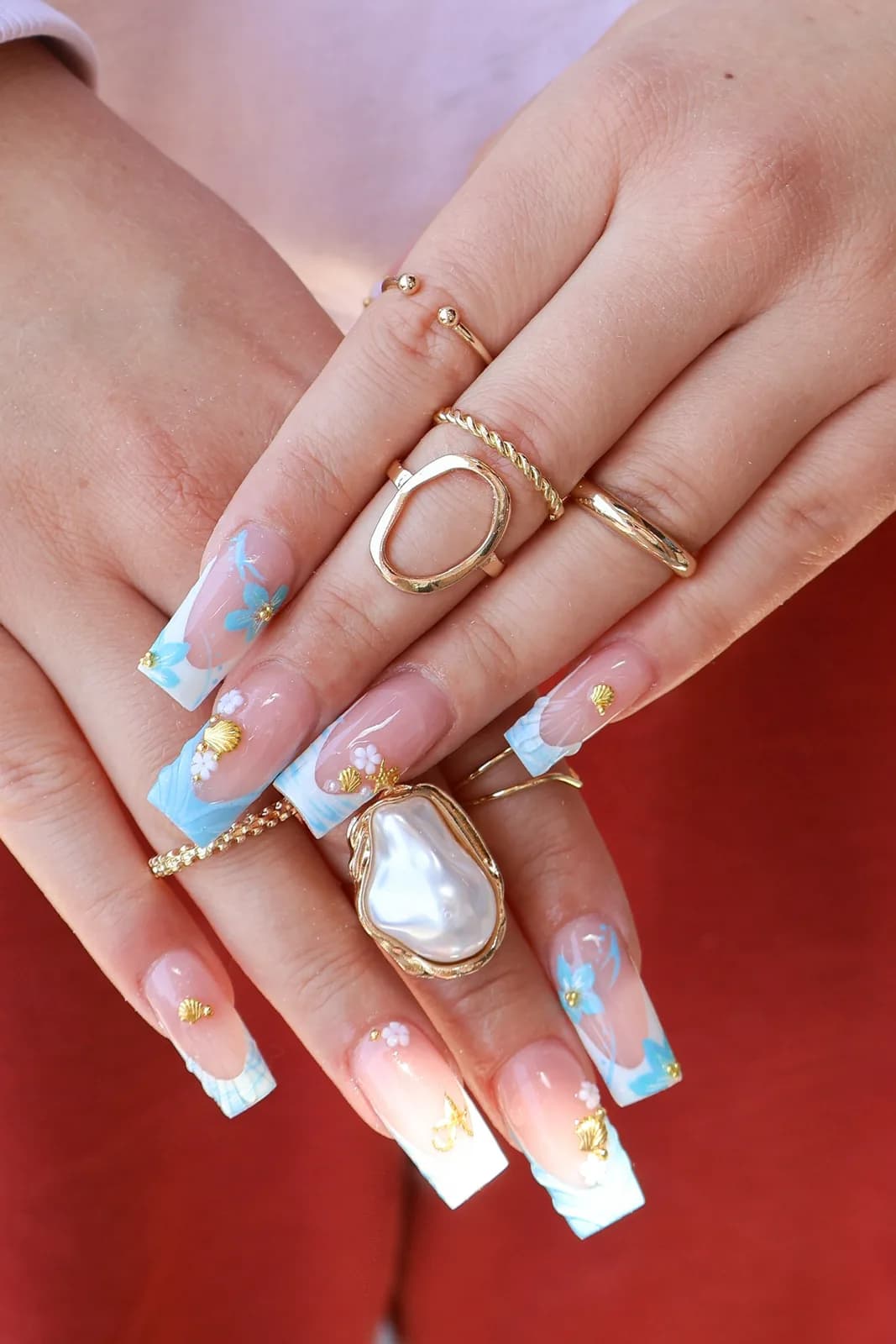 Sky-blue French nails with gold foil and white flowers, styled with gold rings