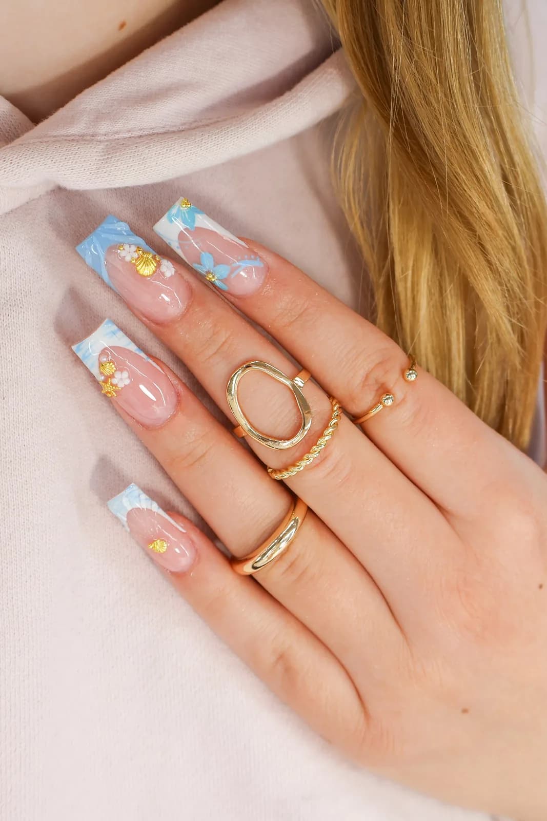 Light blue French square nails with gold flakes, worn with a cream hoodie