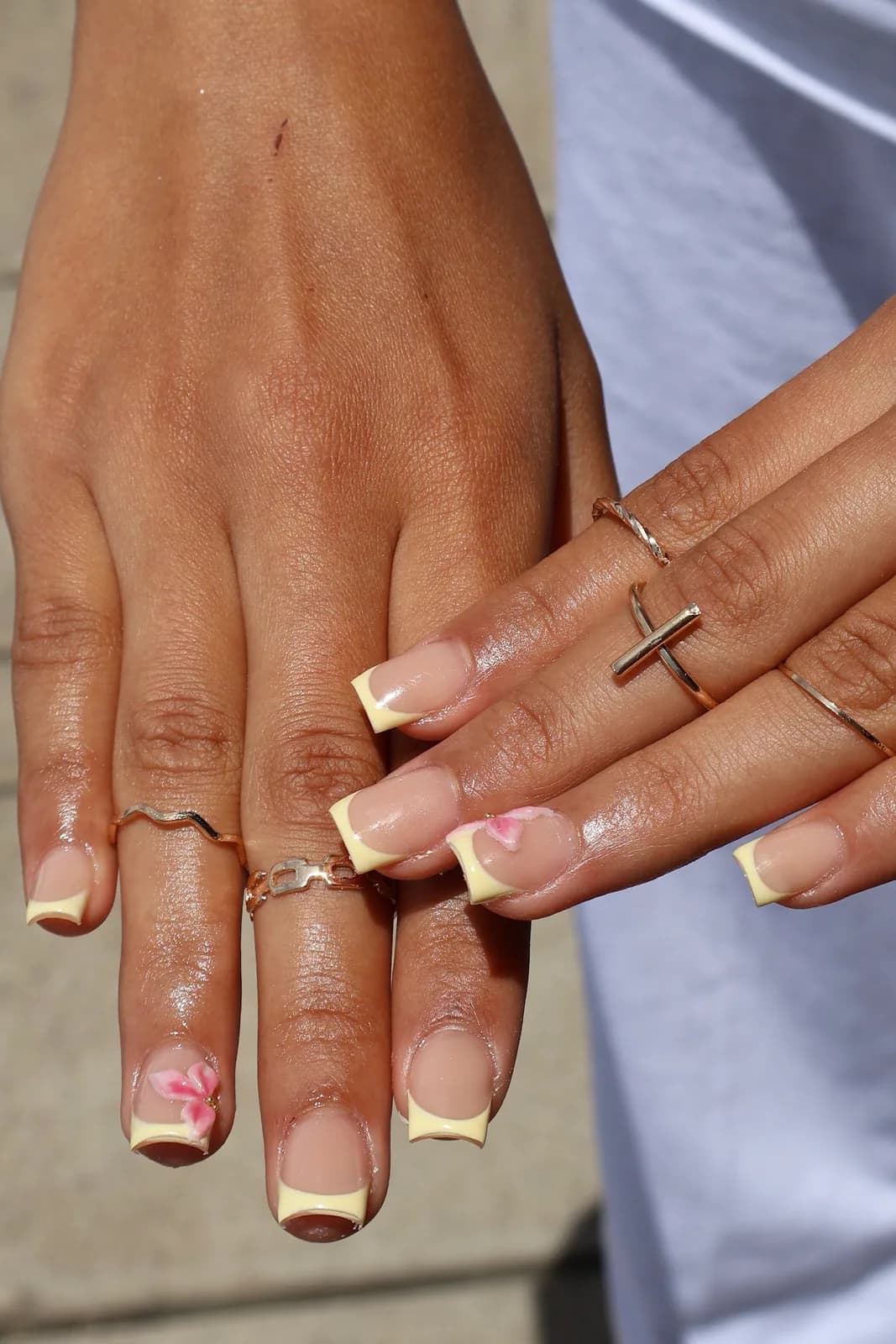 Butter-yellow French tip nails with a tiny pink flower, photographed outdoors
