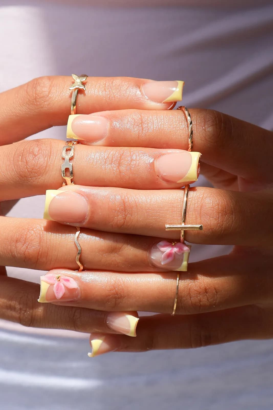 Butter-yellow French manicure styled with layered gold rings