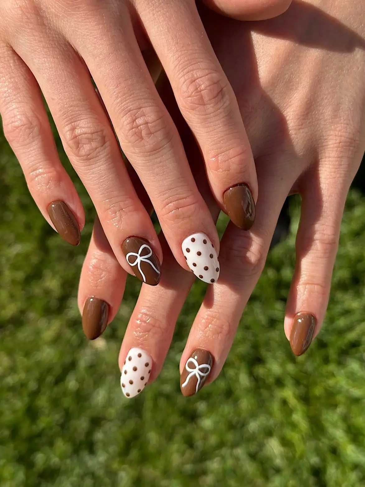 Almond nails in glossy chocolate brown with white bow accents and white nails with brown polka dots