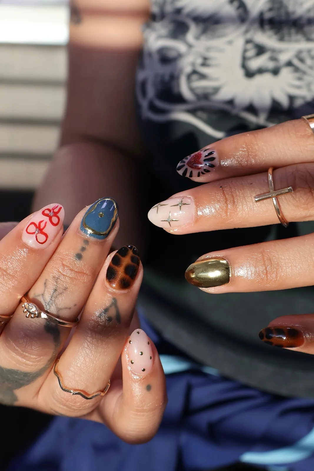 Both hands showing mismatched designer-inspired nail art with chrome accents