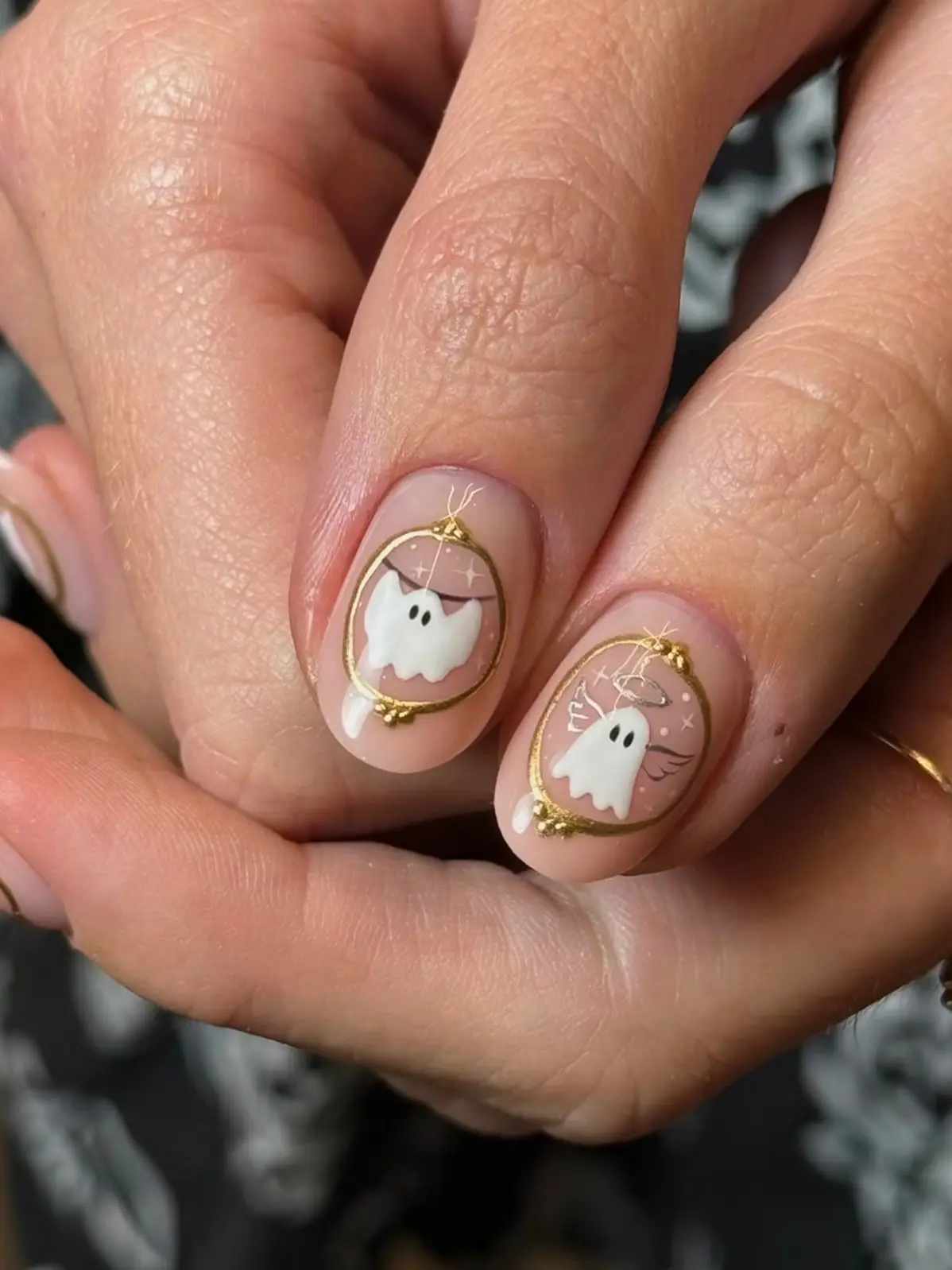 Clasped hands showing gold-framed ghost Halloween nails with tiny sparkle details