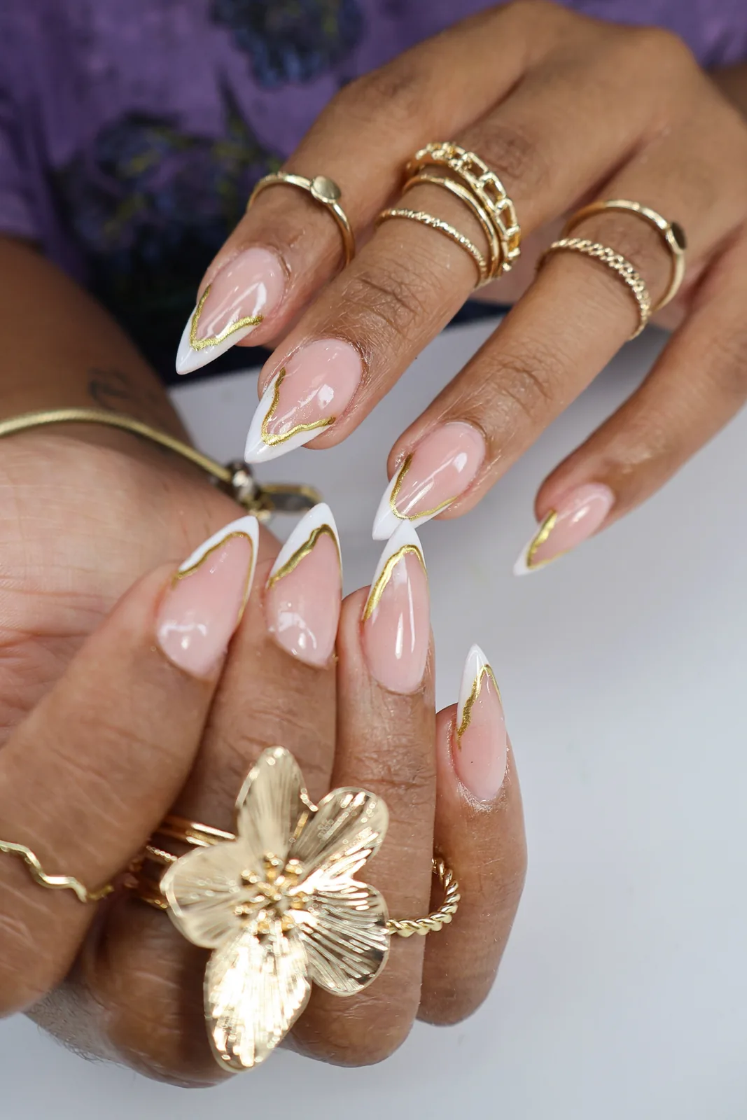 Gold-outlined French stiletto nails styled with stacked gold rings