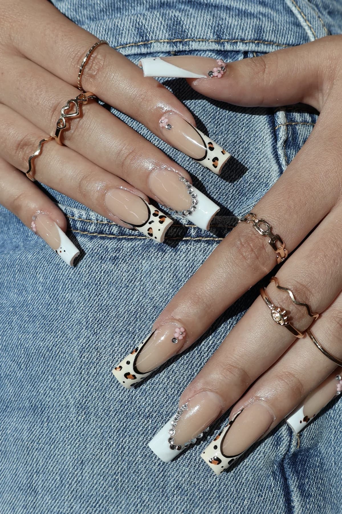 Long coffin nails with white leopard French tips and rhinestones on denim