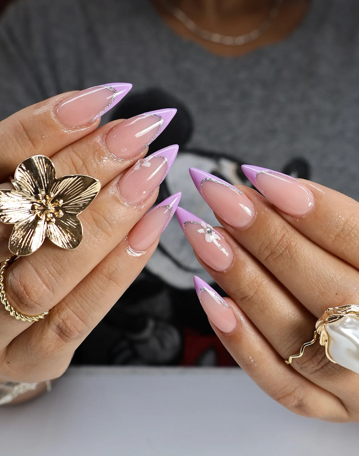 Lilac French stiletto nails with fine glitter, styled with a gold flower ring