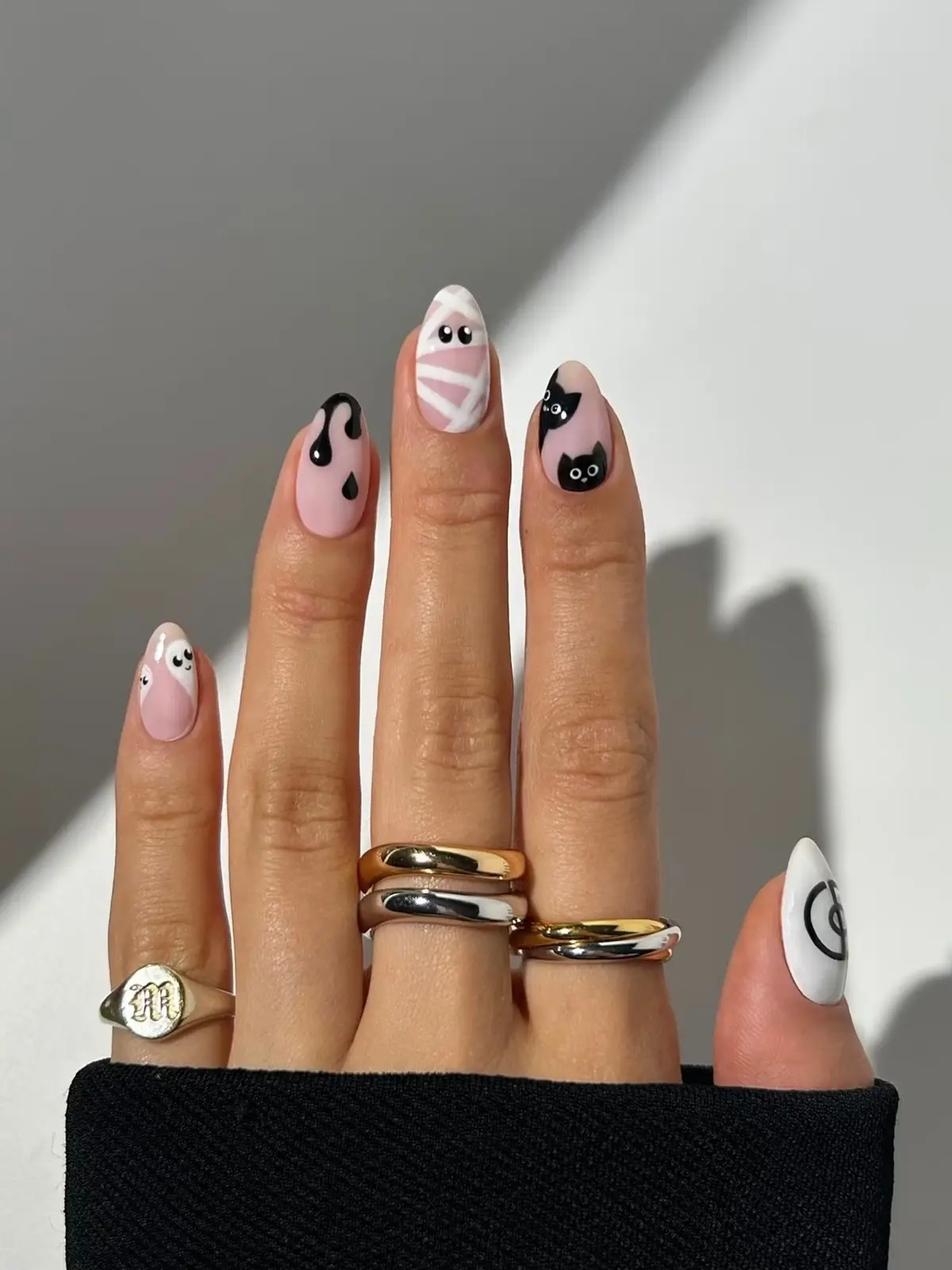 Almond nails with a mummy wrap, black drips, peeking black cats and a ghost duo on a soft pink base