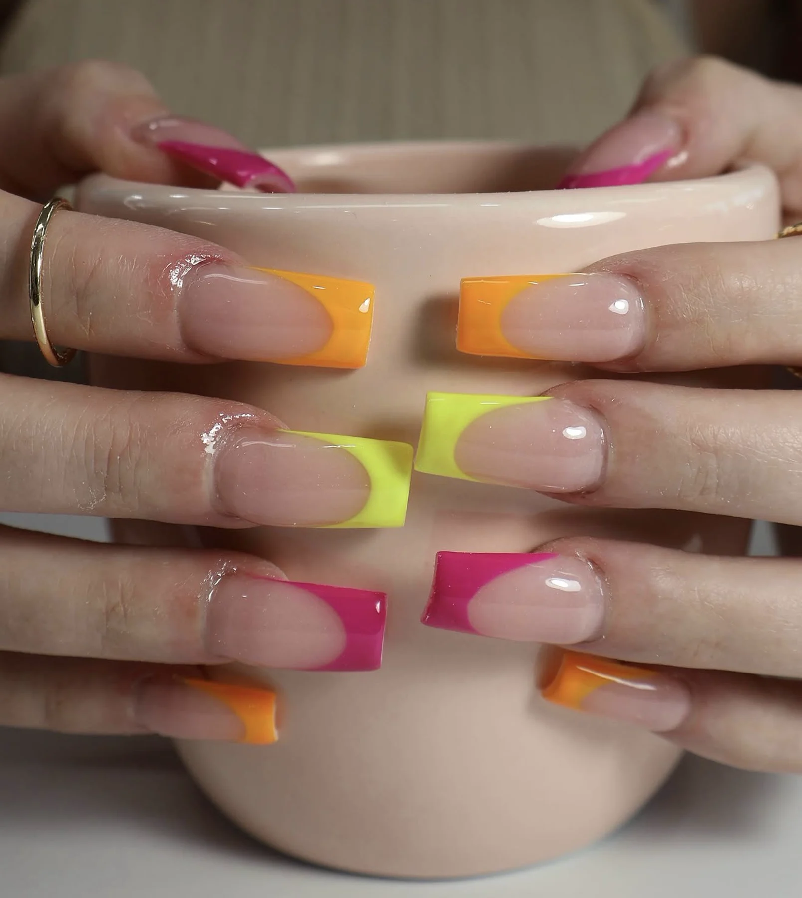 Square nails with neon pink, orange, and yellow French tips around a mug