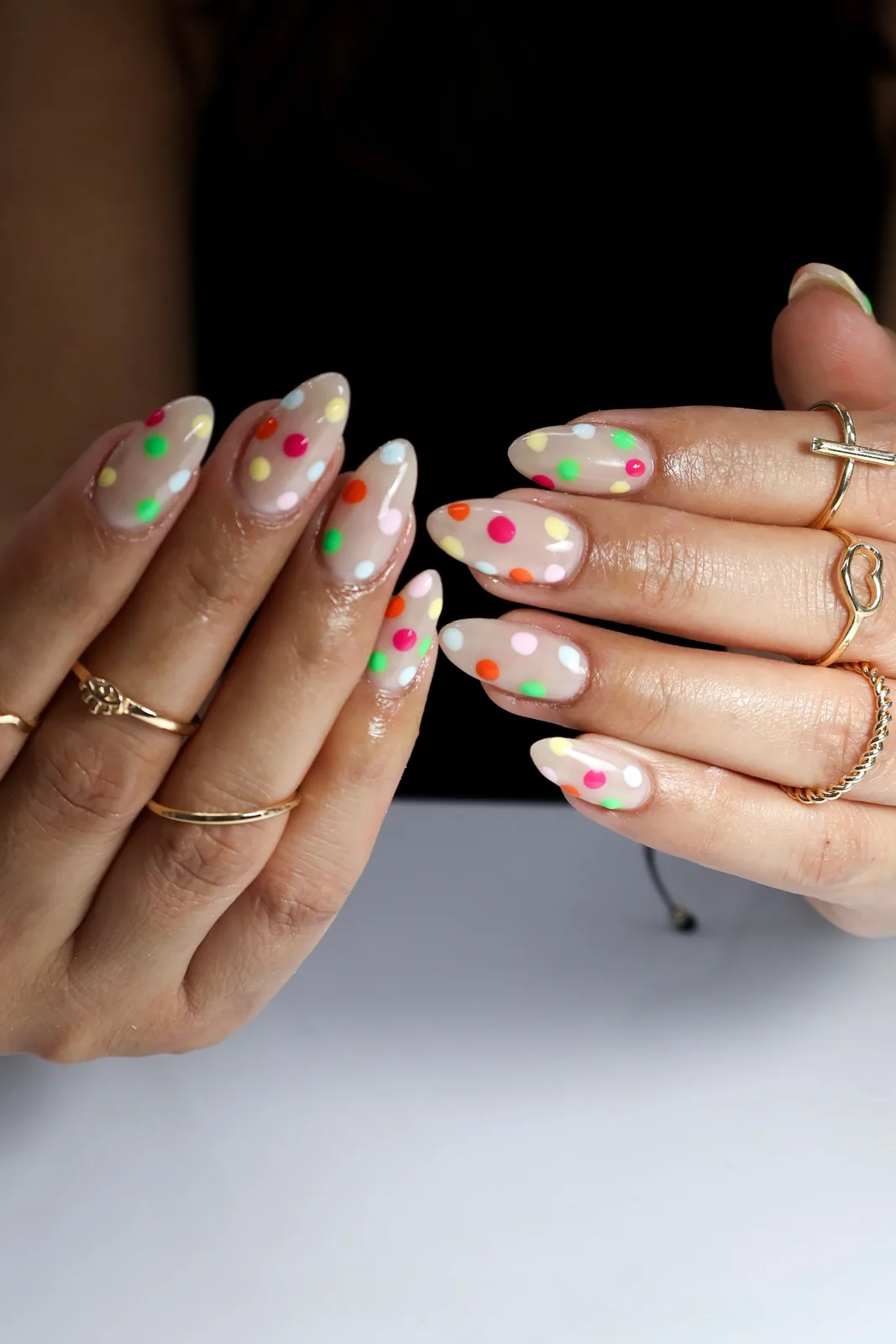 Both hands showing milky white almond nails with rainbow polka dots