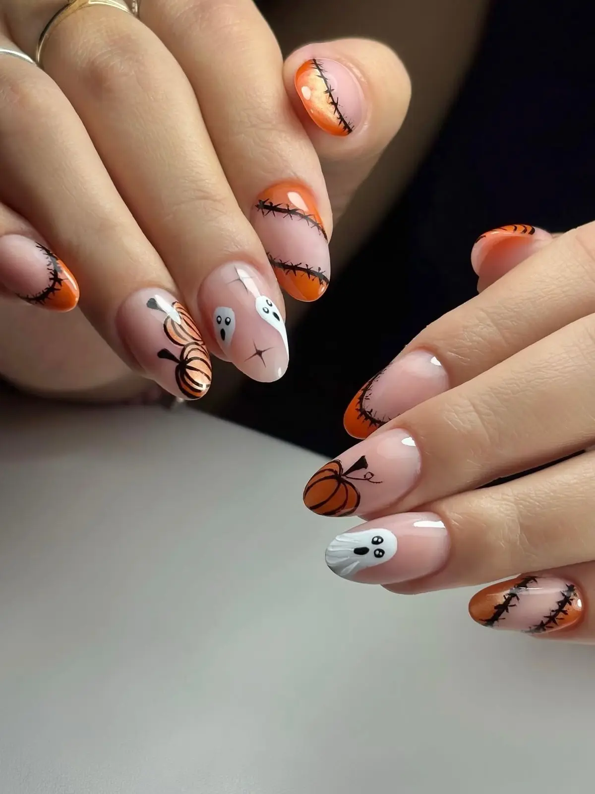 Orange shimmer French tips with black Frankenstein stitches, line-drawn pumpkins and small ghosts