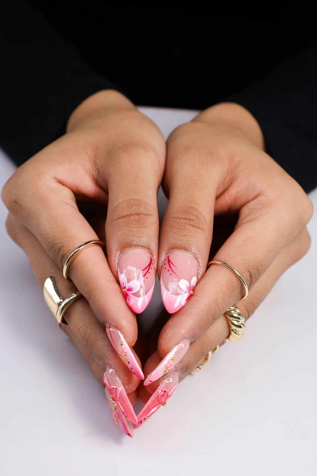 Hands posed together showing sheer pink almond nails with white flower art