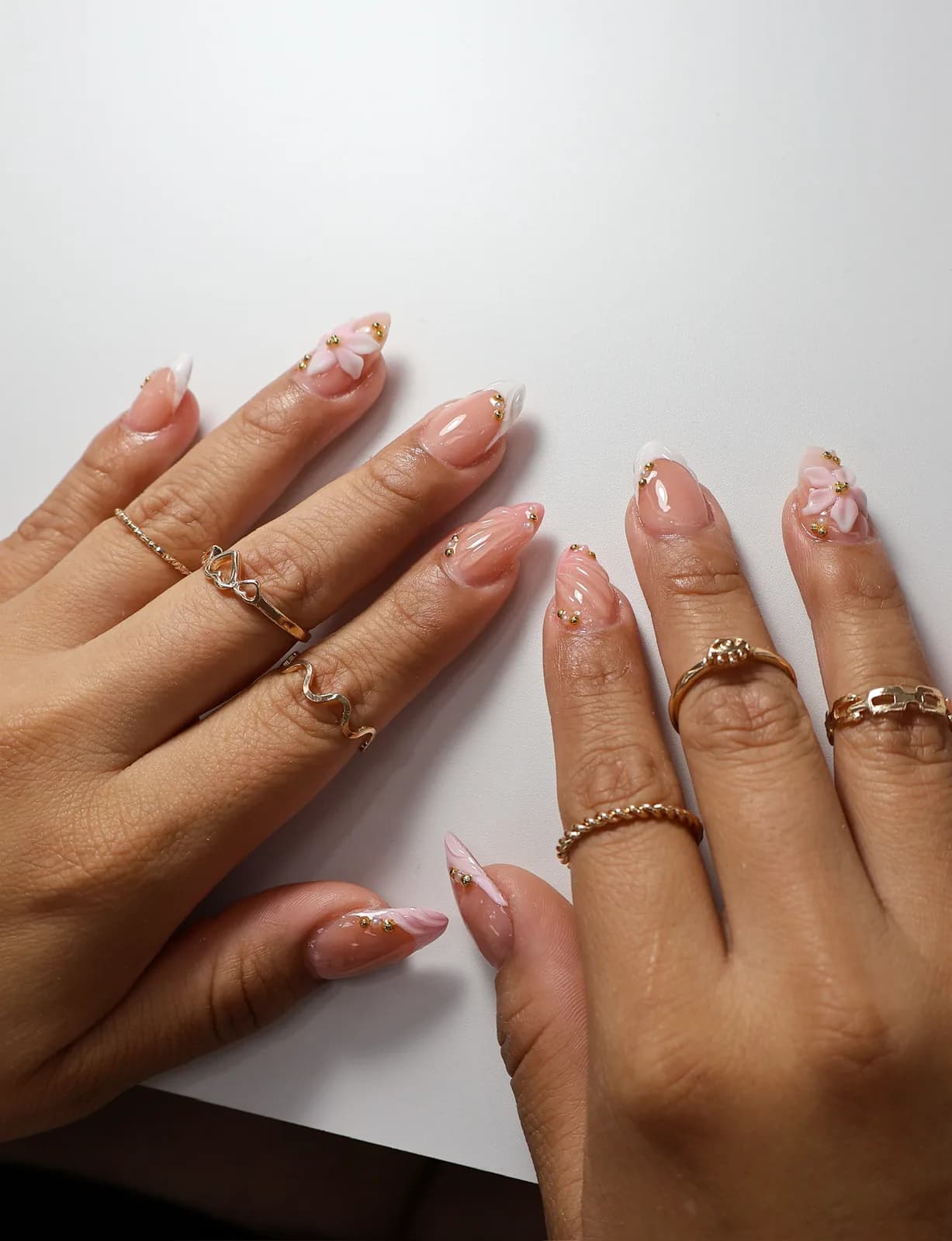 Hands resting on a table showing pink flower French nail art