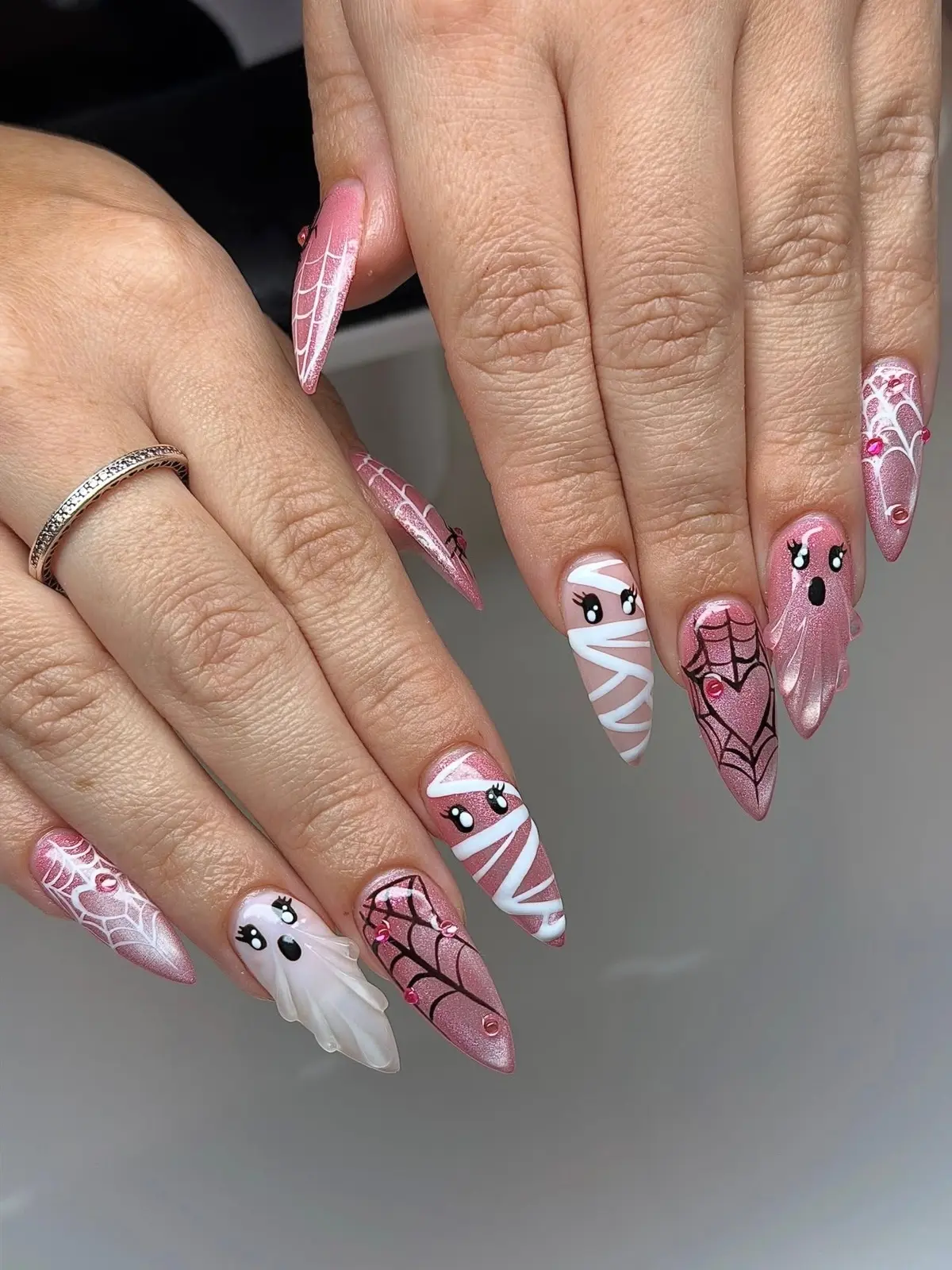 Both hands with pink Halloween stiletto nails featuring white mummy wraps, sculpted ghosts and spiderwebs