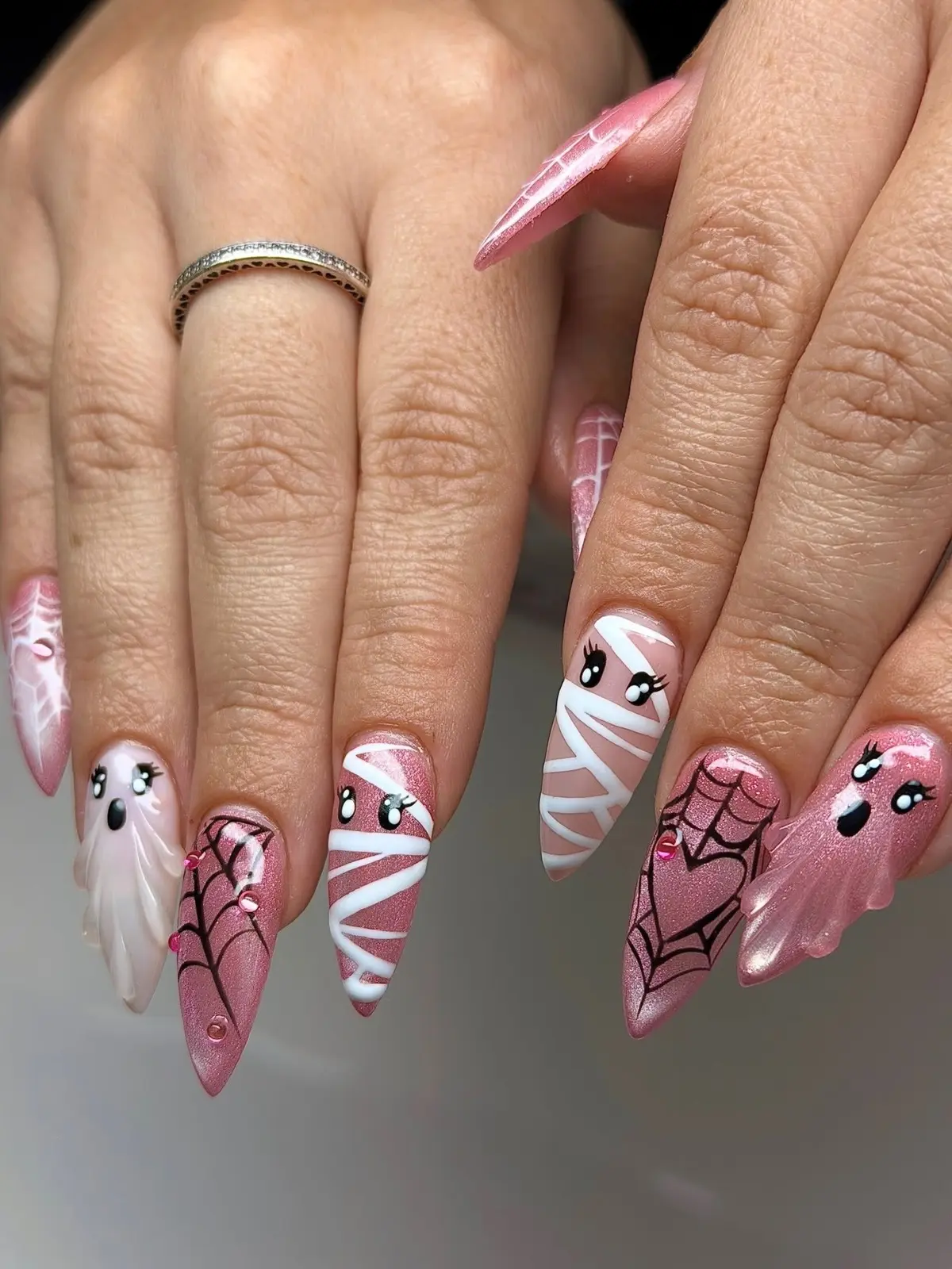 Long pink shimmer stiletto nails with lashed mummies, sculpted ghosts, black spiderweb hearts and pink gems