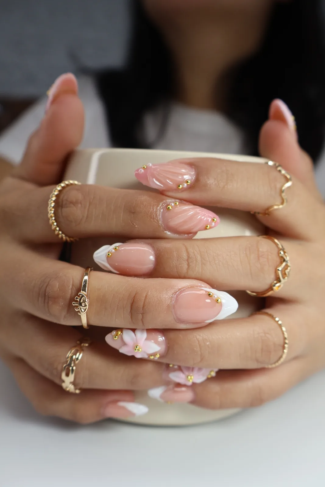 Pink and white French nails with seashell texture and pearls holding a cream mug