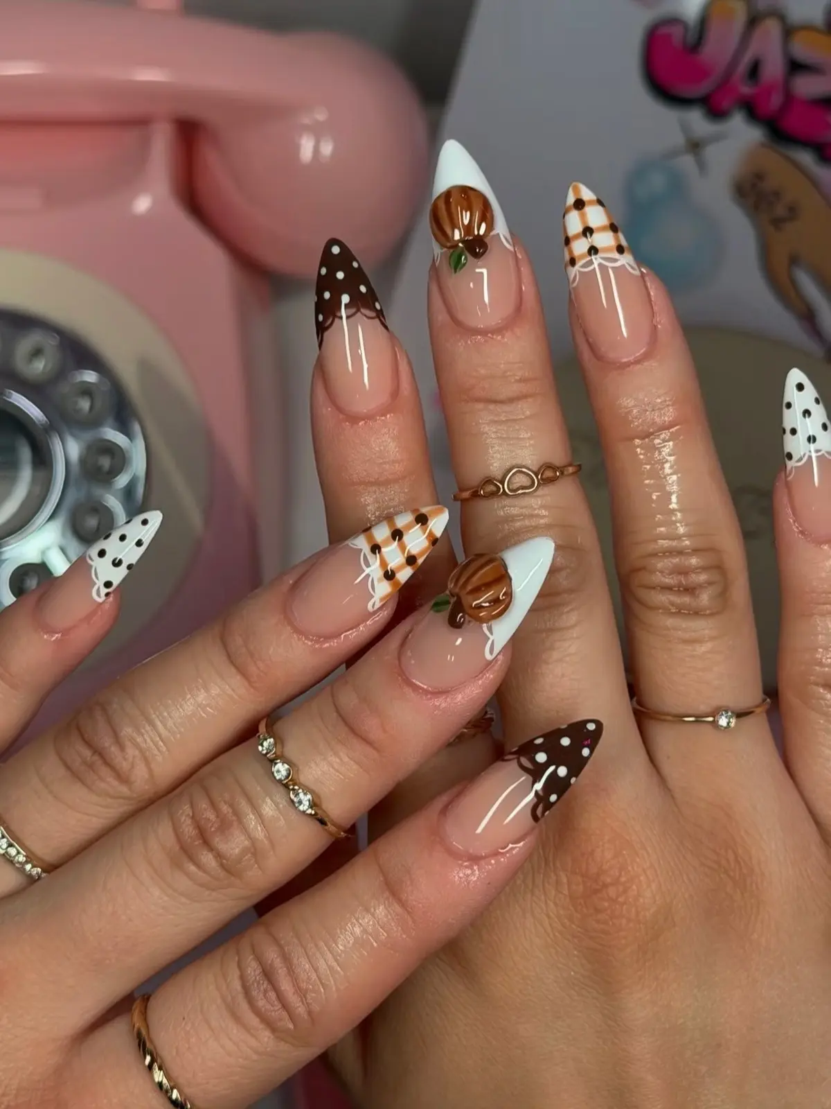 Stiletto fall nails with brown and white polka-dot tips, plaid accents and a pumpkin on white French