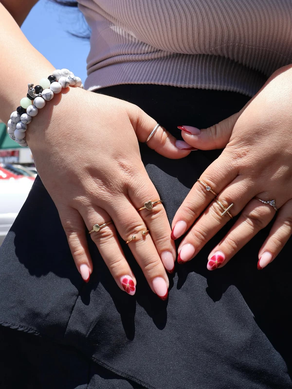 French tip nails with red pressed-flower accents, photographed outdoors