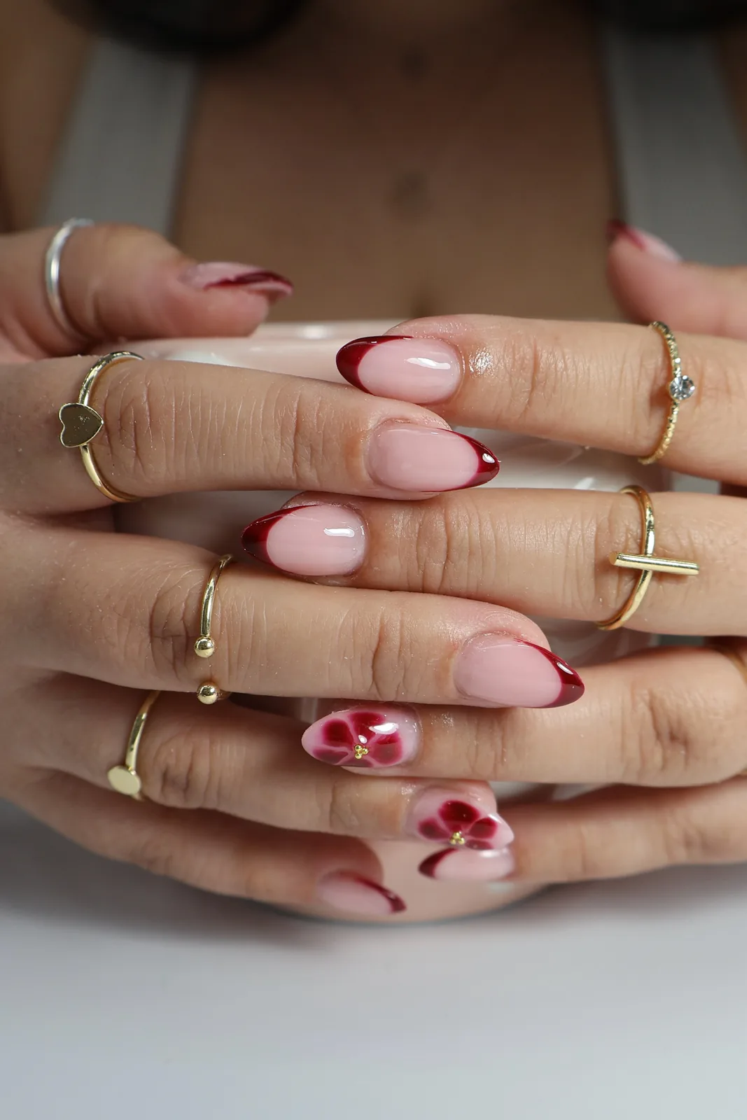 Deep red French almond nails with painted rose accents holding a mug