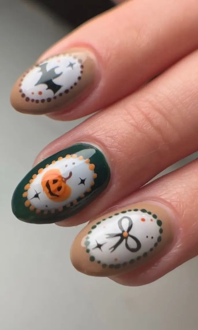 Close-up of cameo-framed nail art with a bat, a jack-o’-lantern and a bow on caramel and forest green nails