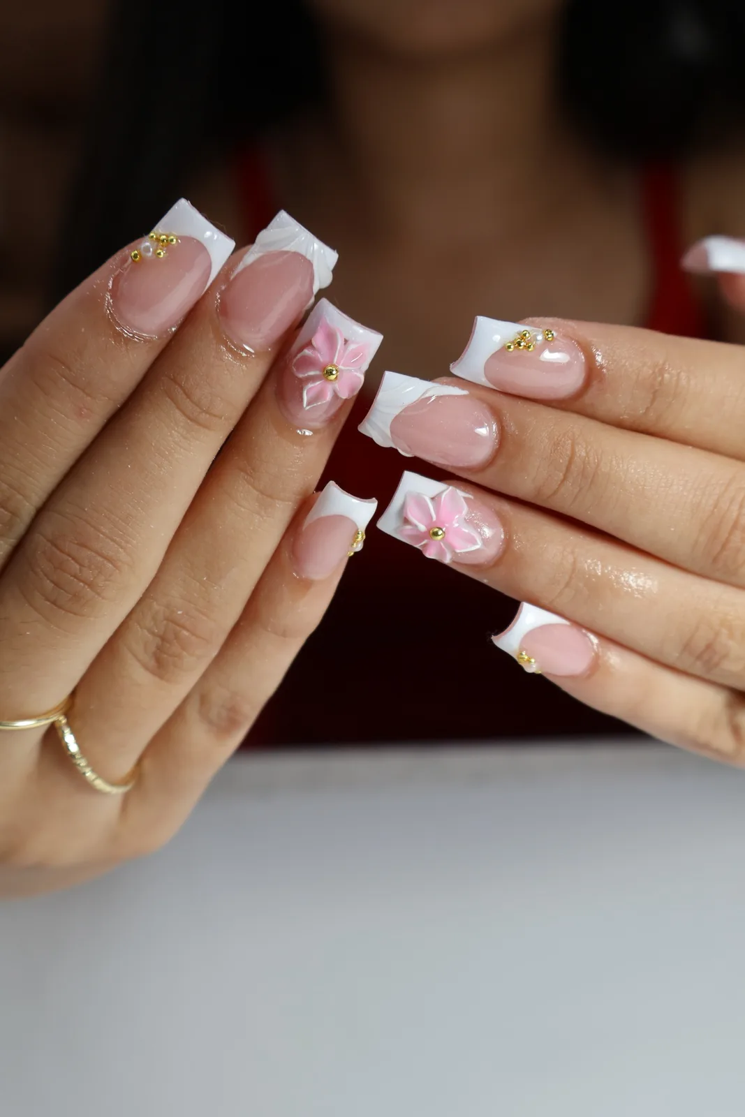 Both hands showing white French tips with sculpted pink flower nail art