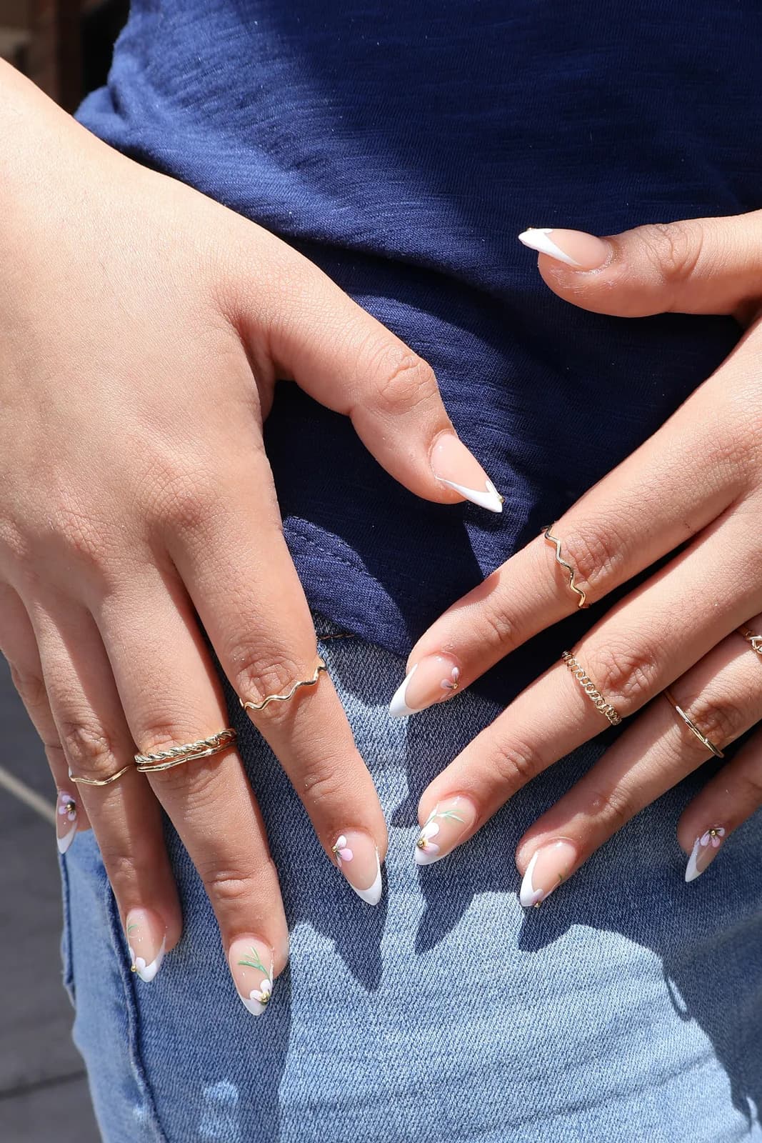 White French manicure with delicate leaf art, hands resting on jeans