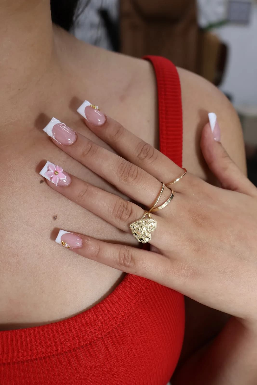 White French square nails with a pink bow accent, resting on a red top